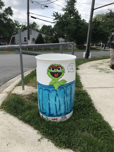 A white, plastic garbage can with a green Oscar the Grouch painted on the side.