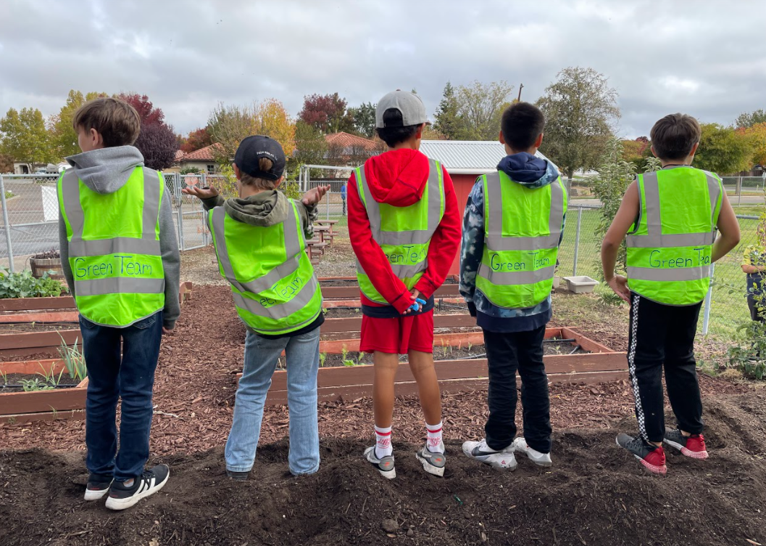 Five students wearing green vests look out over a garden.