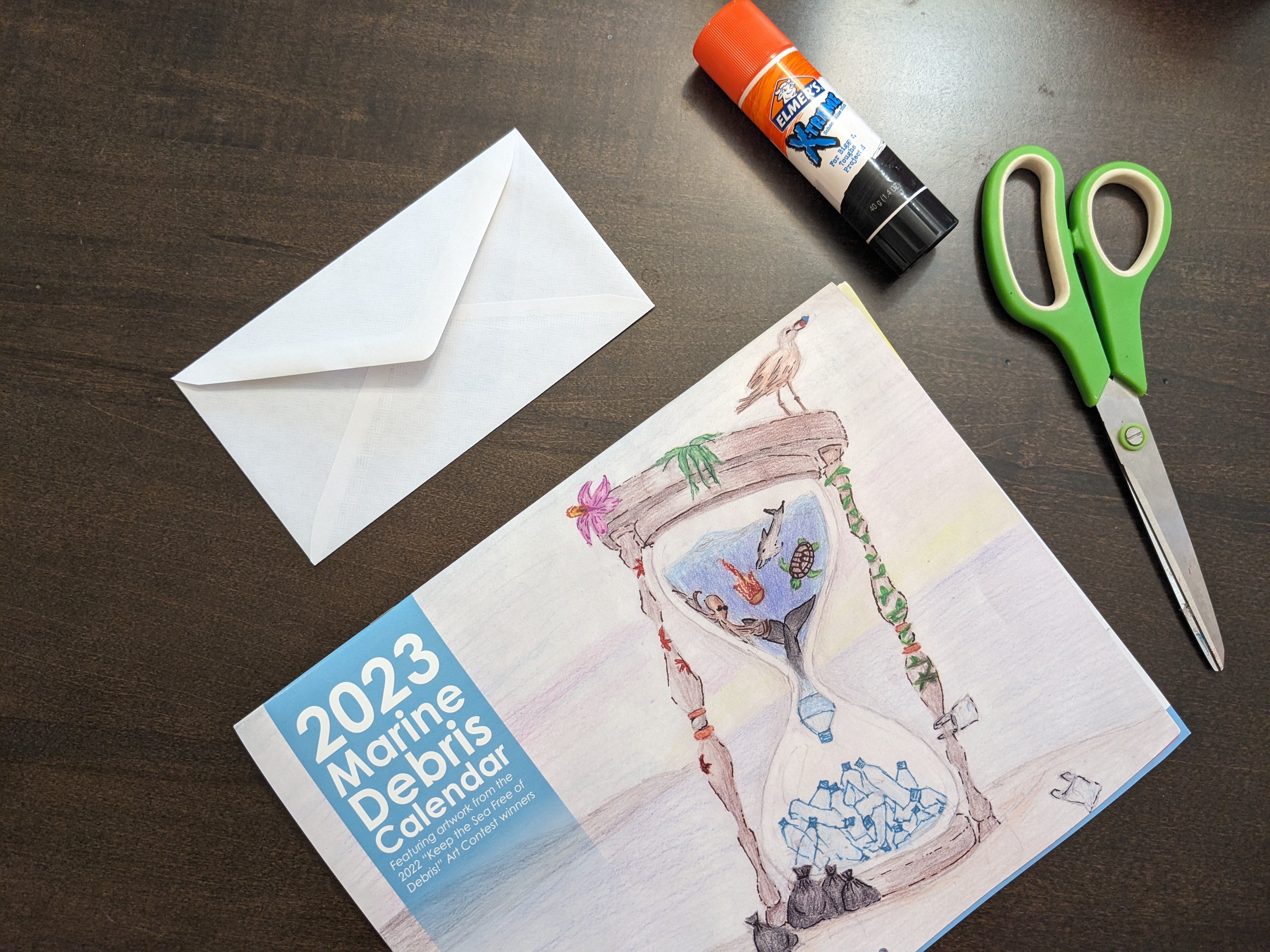 A calendar, envelope, glue stick, and pair of scissors on a table.