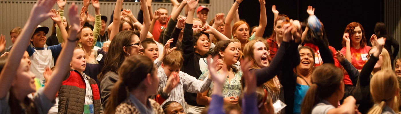 Many students raising their hands in an auditorium.