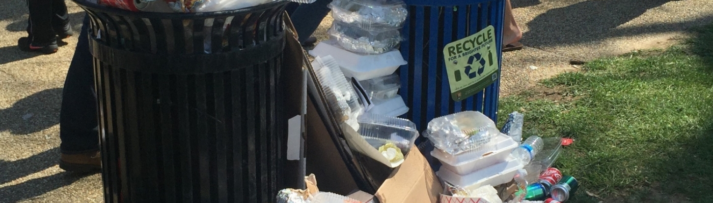 A trash and recycling can overflowing with single-use food containers at an outdoor event.