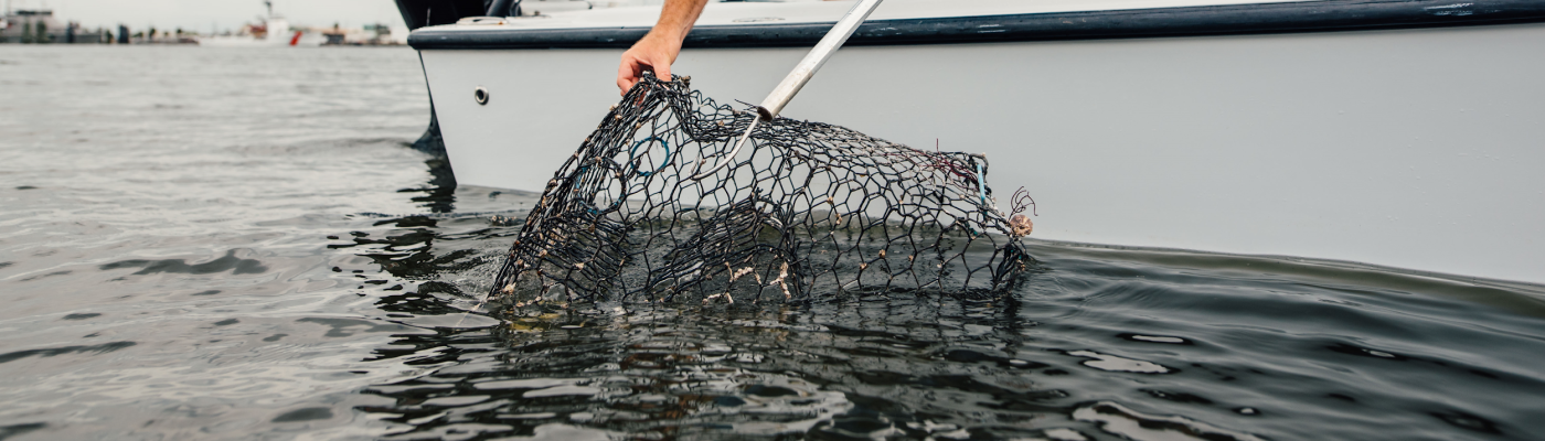 A person pulling up a crab trap on a boat.