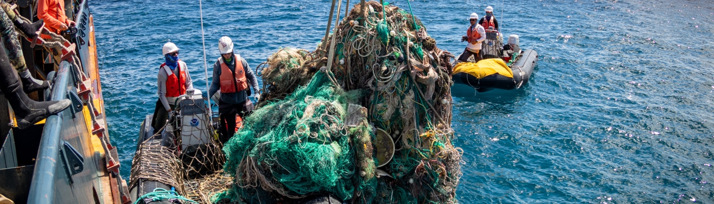 A marine debris removal team member offloads a huge mass of derelict fishing net from a boat.