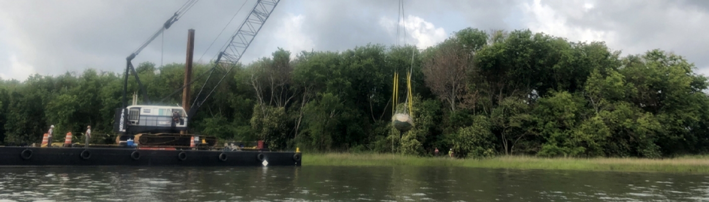 A sailboat being lifted by a crane out of a marsh.