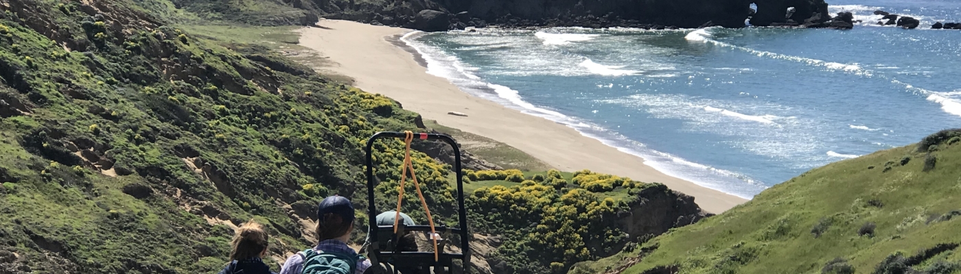 Three people hiking together through hills overlooking an ocean beach.