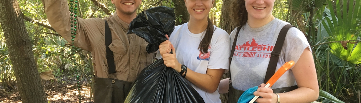 Project participants holding a bag of collected debris as well as collected Mardi Gras beads.