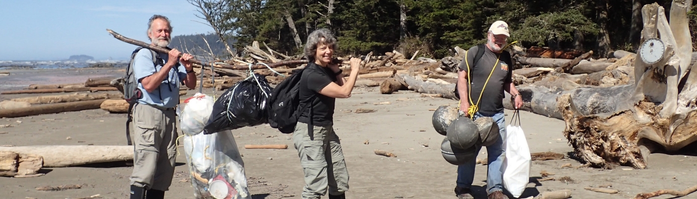 Three people carrying marine debris off a beach.