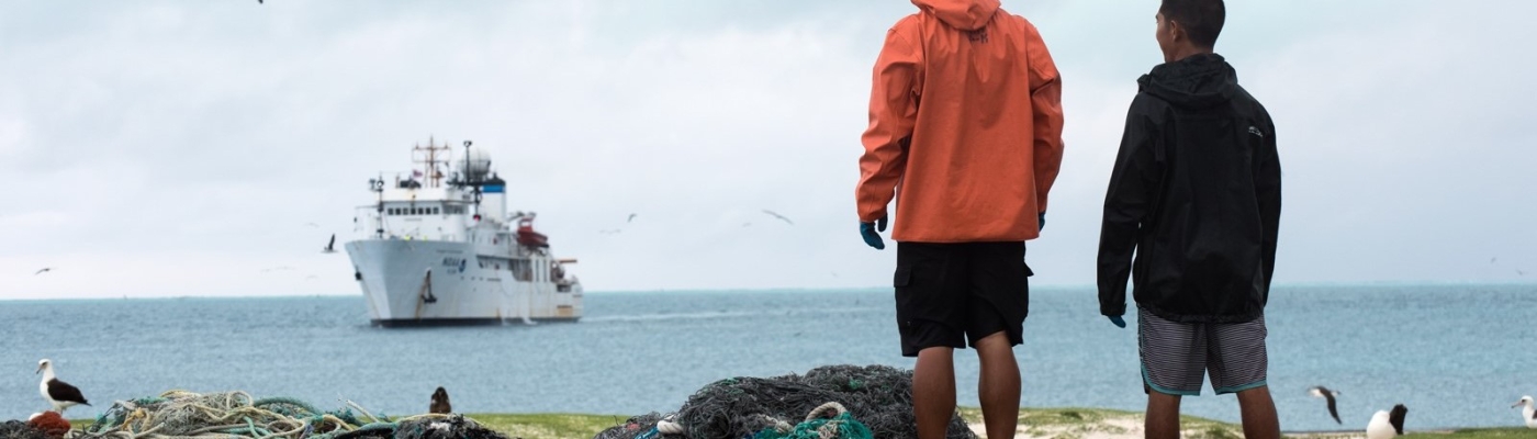Two team members stand next to a pile of collected derelict fishing nets during the 2016 removal mission.