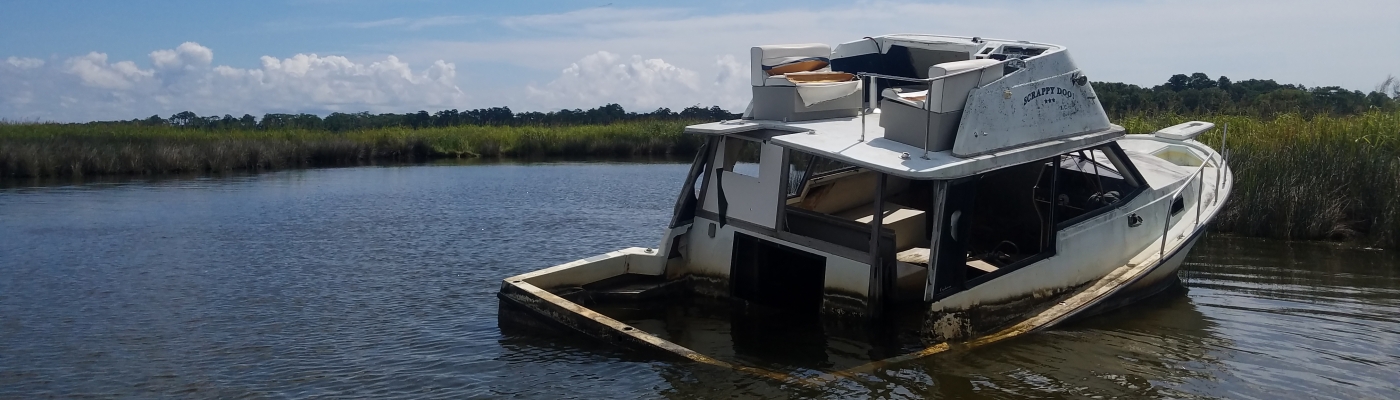 An abandoned and derelict vessel partially submerged and stuck in a marsh.