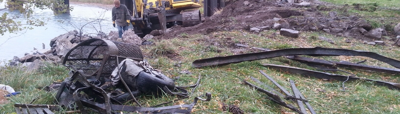 A man surveys large debris items with a crane in the background.