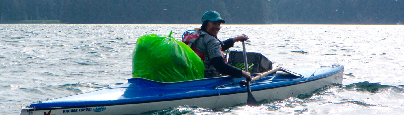 A volunteer in a kayak with a bag of debris.