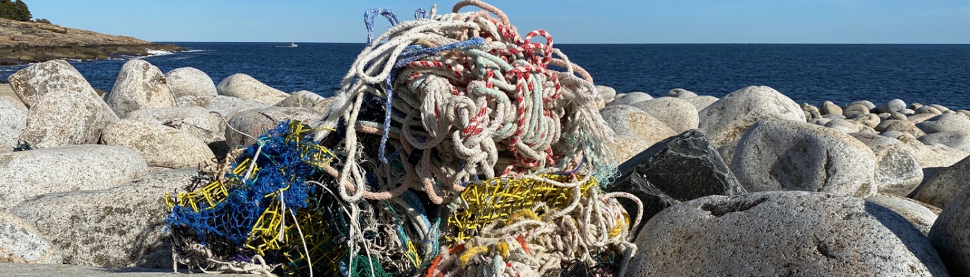 A mound of ropes, net, and other fishing gear piled on a rocky shoreline.