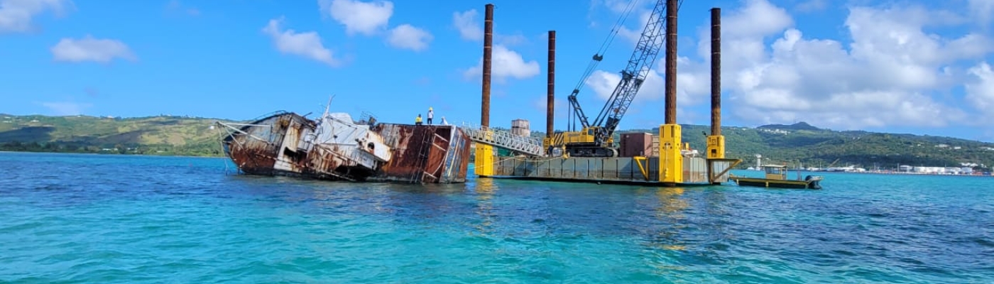 A large vessel sits with its side resting partially underwater with a crane and platform next to it. 