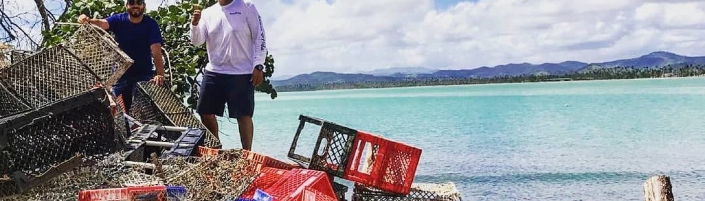 Two men stand on a beach next to a pile of collected crab traps.