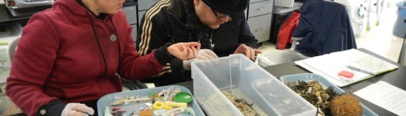 Two teachers sort through a bin of marine debris in a lab. 