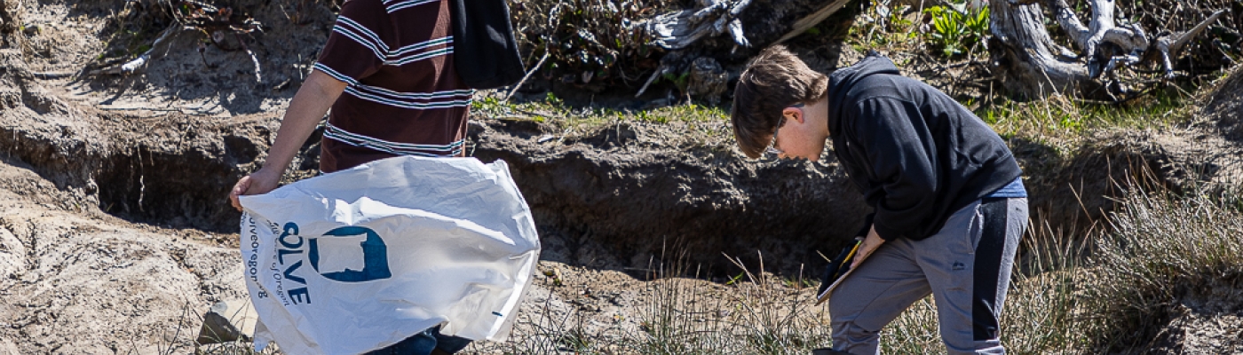 Two students survey for debris among rocks and driftwood. 