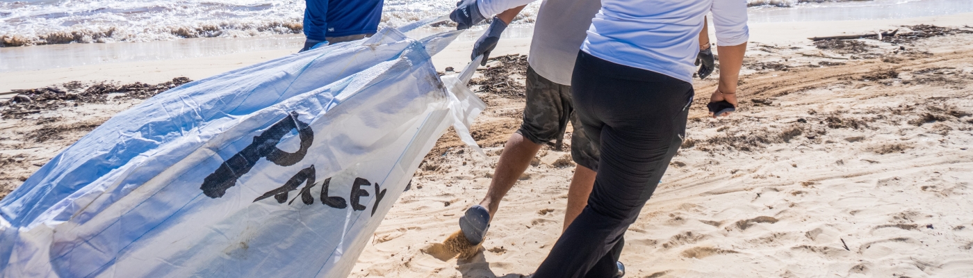 Three people carry a large bag down the beach during a cleanup.