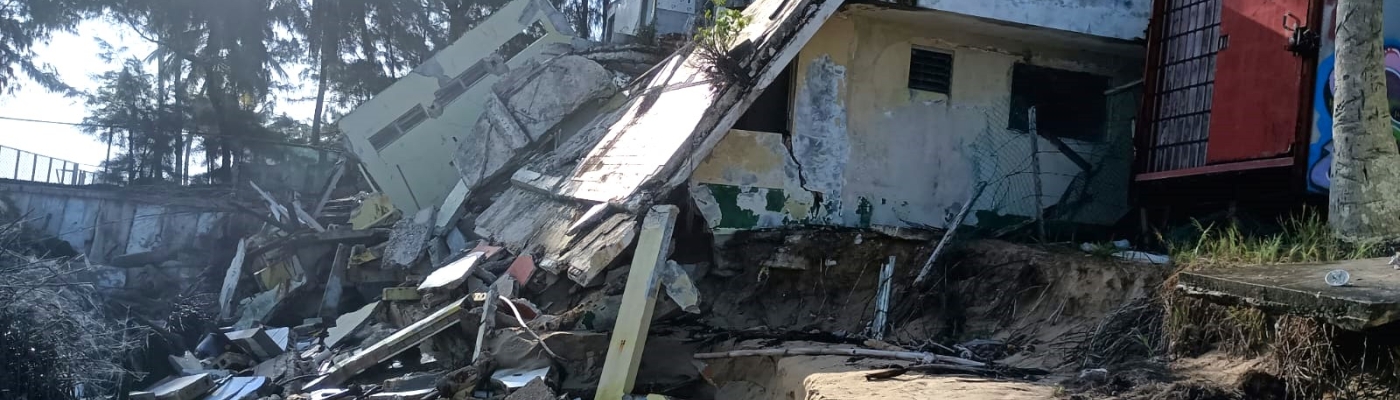 A dilapidated house structure on a tropical, sandy shoreline.