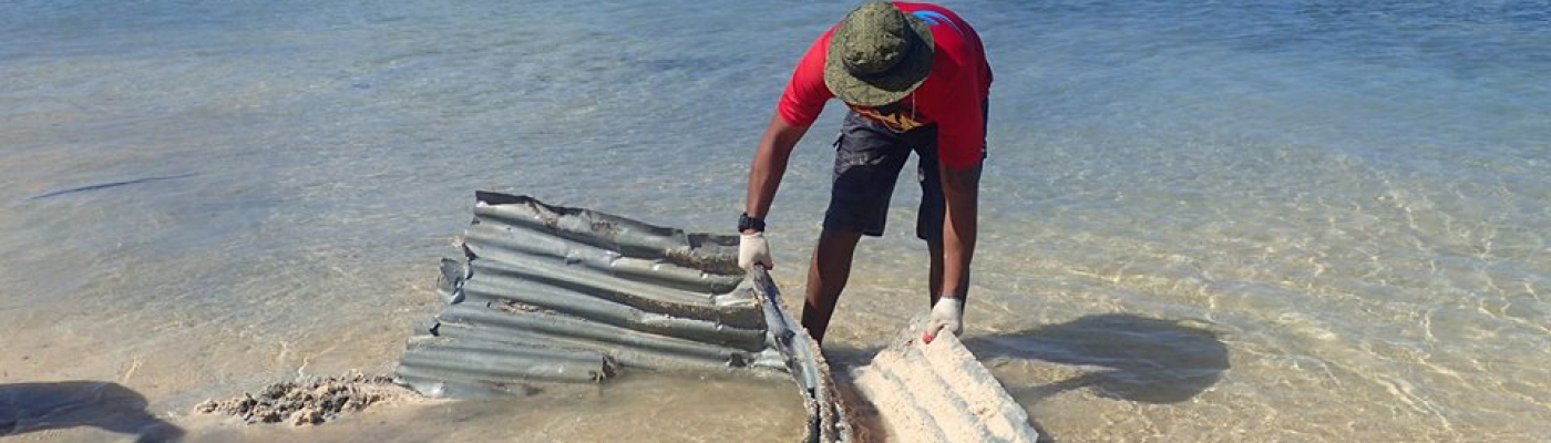 A volunteer removing corrugated roofing tin from an ocean shore.