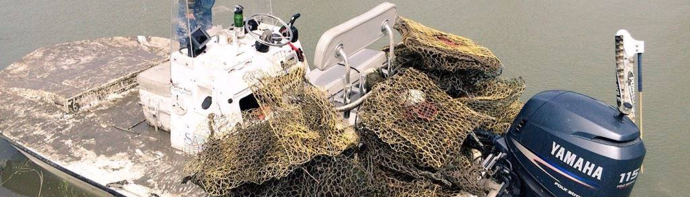 A person stands on a small vessel that is loaded up with derelict fishing traps.