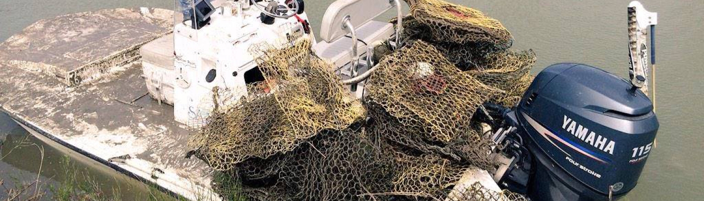 Man standing at the front of his boat with a pile of derelict crab traps piled at the rear.