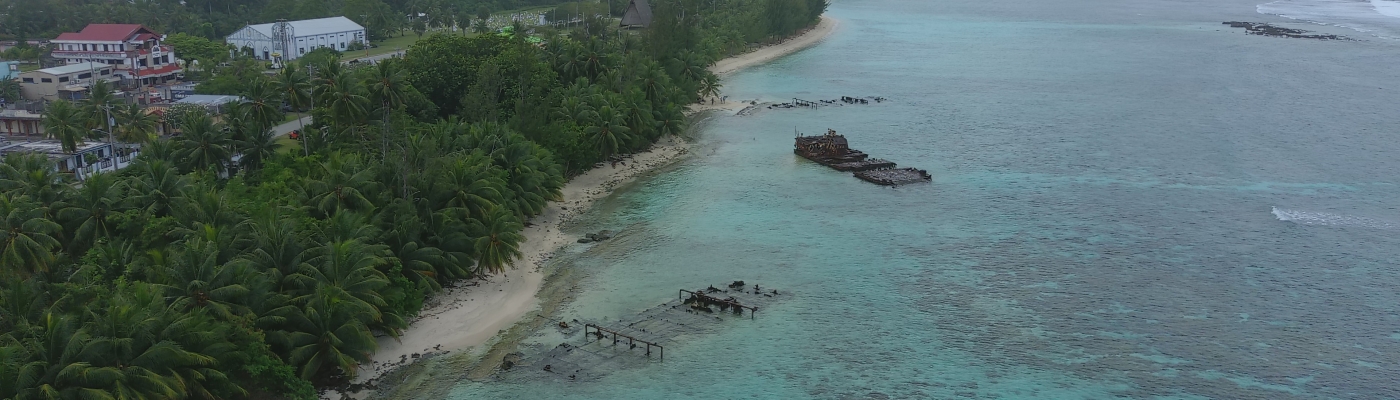 Three derelict vessels partially submerged close to a beach.