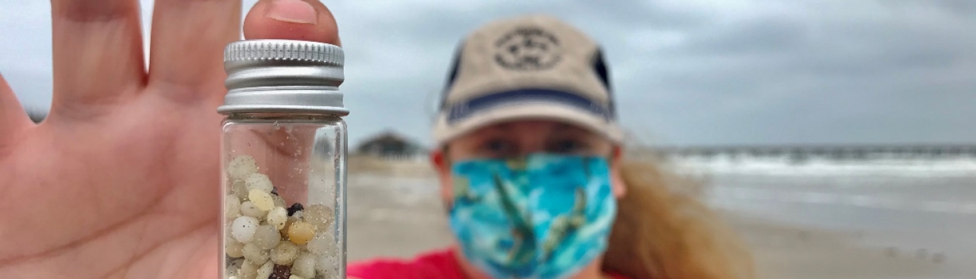 Nurdle Patrol citizen scientist holding up a small jar full of plastic pellets, or nurdles, collected on the beach.