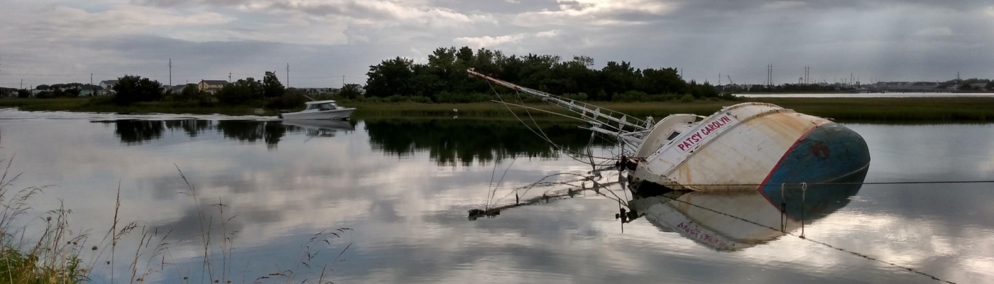 A derelict vessel on its side and partially submerged in the water.