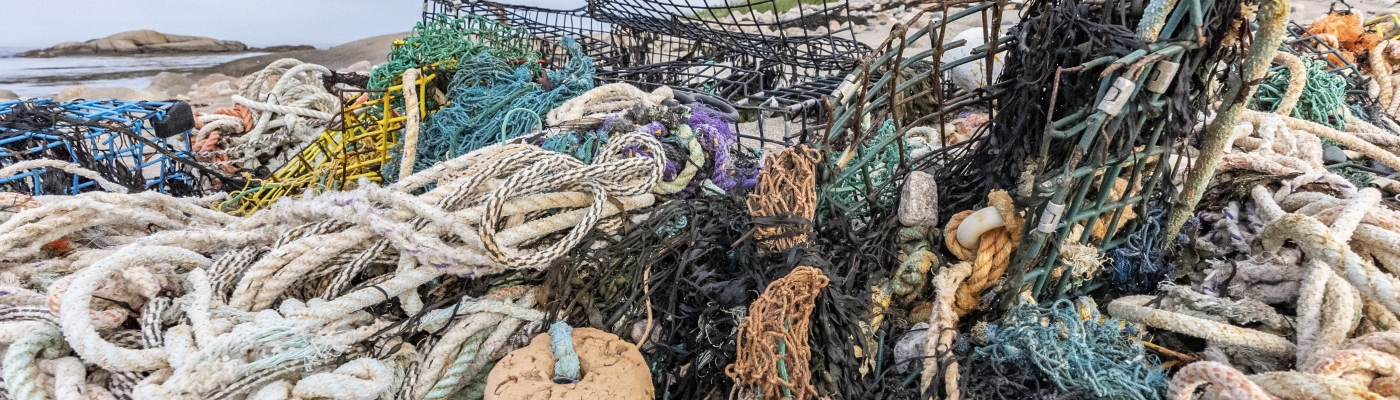 A pile of colorful fishing rope, buoys, and fishing traps are abandoned and sprawled across a coastline with a rocky outcropping in the background.