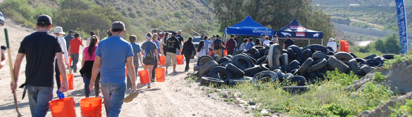 Volunteers with orange buckets walking up a dirt road past a pile of old tires.
