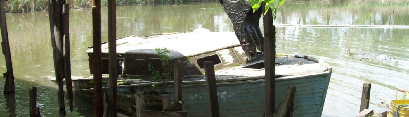 Derelict vessel in waterway being removed by heavy equipment.