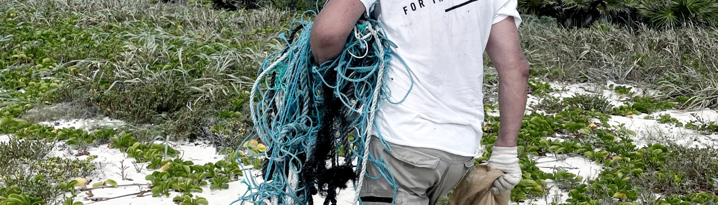 A person on a beach carrying a bag full of debris and a small mass of derelict fishing nets.