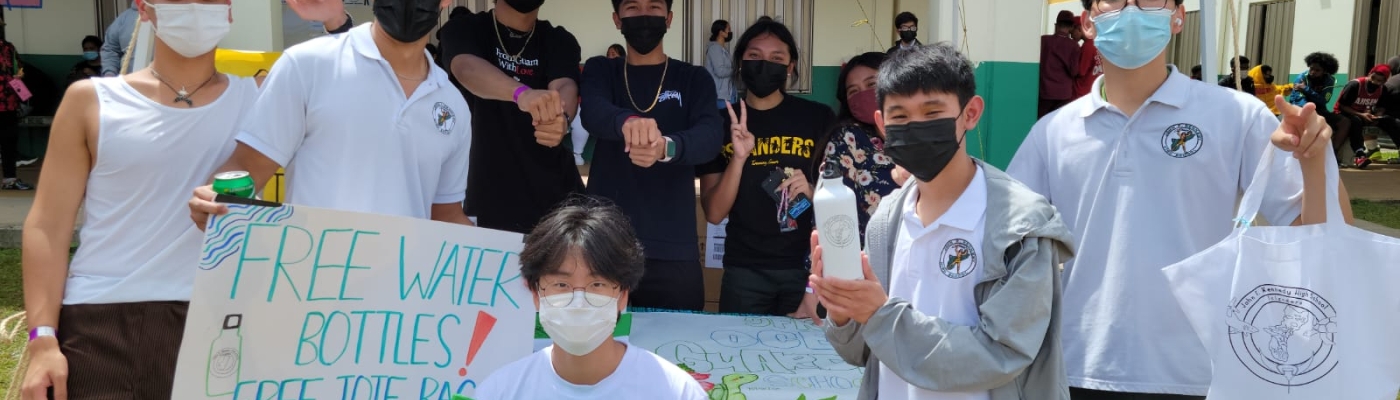 Students handing out reusable water bottles and bags at an outdoor campus event.
