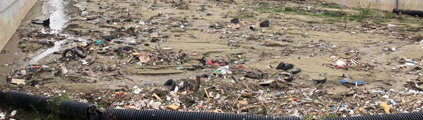 Trash along a muddy riverbed with concrete walls.