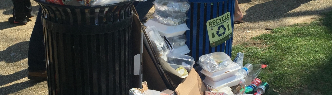 Overflowing trash cans with plastic and styrofoam garbage on the ground.
