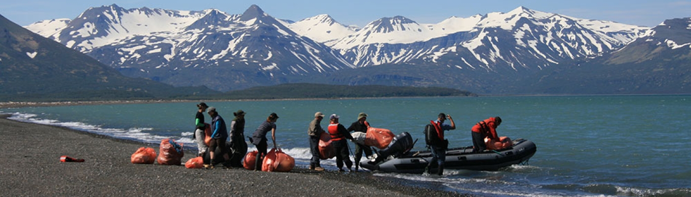 Volunteers loading debris into a boat on a remote Alaskan shoreline. 