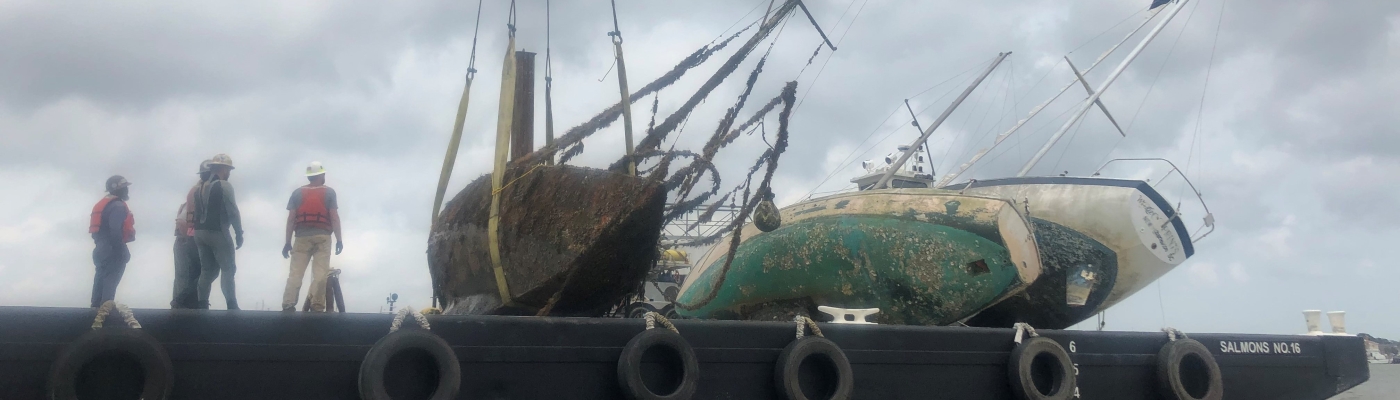 People watch as derelict vessels are loaded onto a barge.