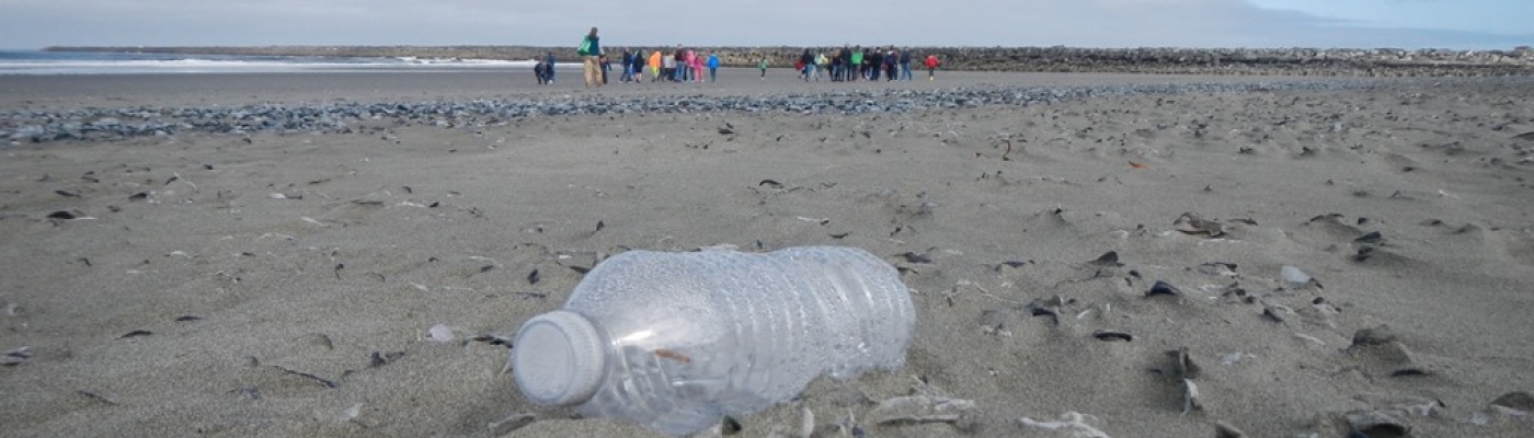 Kids on the beach with plastic bottle trash in the foreground.