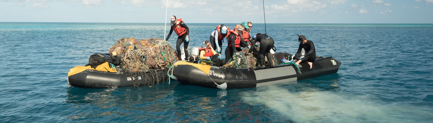 People haul a derelict fishing net into a boat.