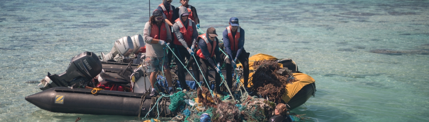 A crew of nine on two small inflatable boats haul a mass of derelict nets out of the water.