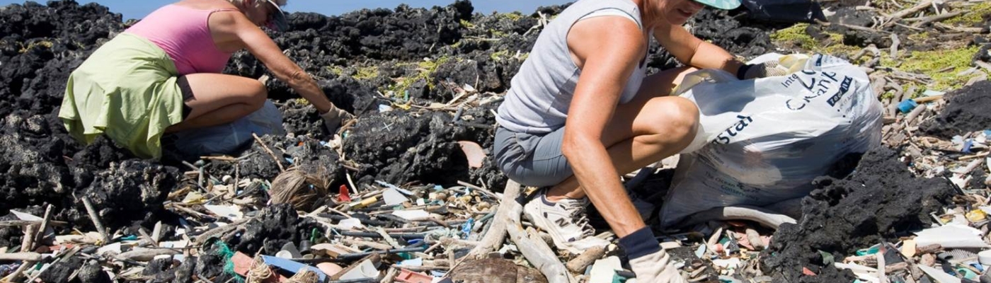 Two people cleaning up marine debris from a rocky shore.