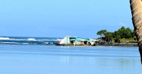 A dilapidated vessel on its side in shallow water near a rocky shoreline.