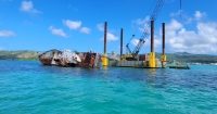 A large vessel sits with its side resting partially underwater with a crane and platform next to it. 