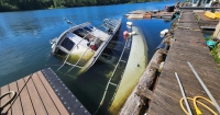 A large vessel lies on its side partially underwater attached to a dock on a sunny day. 