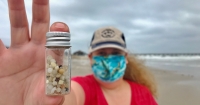 Nurdle Patrol citizen scientist holding up a small jar full of plastic pellets, or nurdles, collected on the beach.