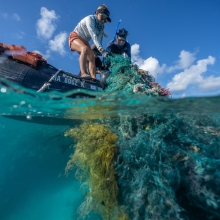 Two people pulling up derelict fishing gear on to a boat.