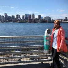 A person stands next to a monofilament recycling bin that is located near the water.