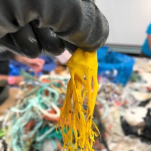 A black, gloved hand holds up a yellow shredded balloon that resembles a jellyfish.