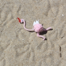 Pink flamingo decoration made out of pipe cleaners on a beach.
