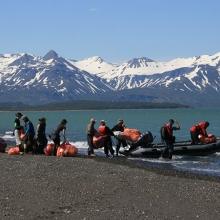 Volunteers loading debris into a boat on a remote Alaskan shoreline. 
